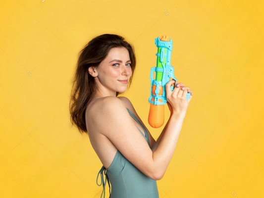 Attractive lady holding a big water pistol against yellow background