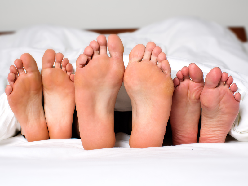 One man and two women lying side by side in bed with feet only showing.